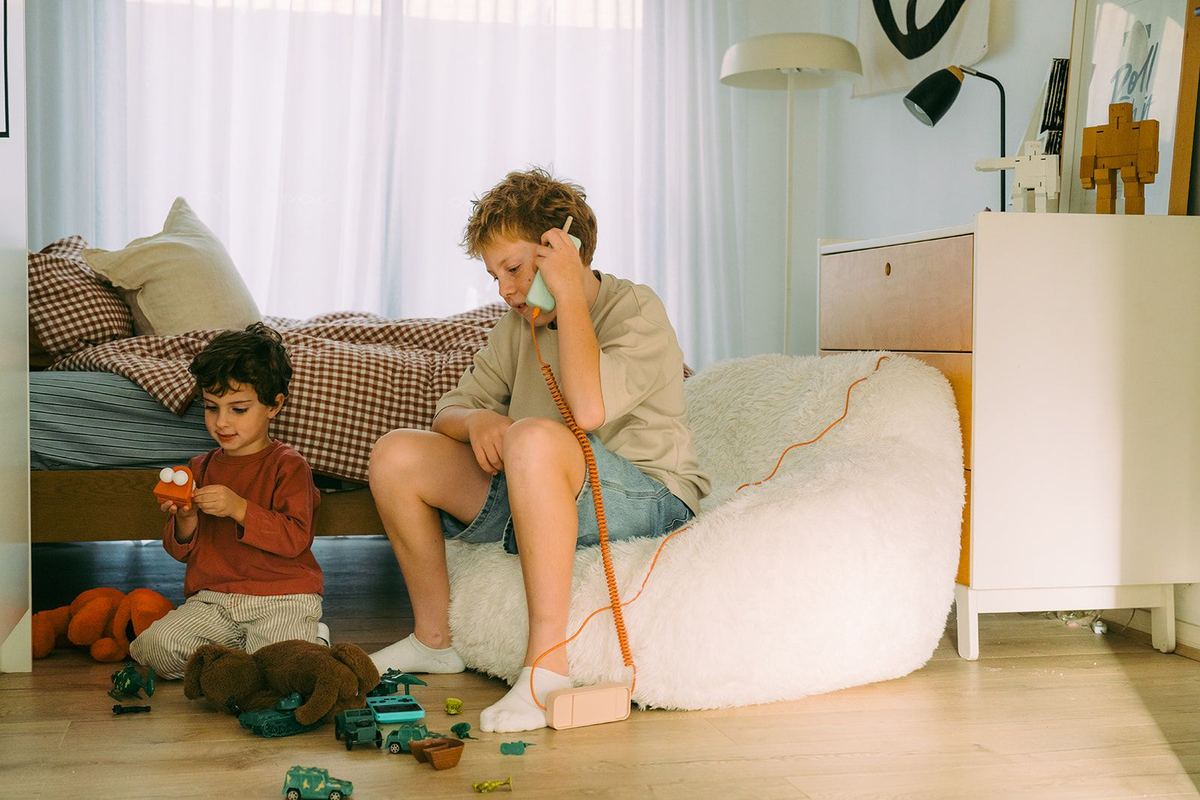 A boy talking on the Waffle Home handset from a beanbag while his little brother plays with toys nearby.