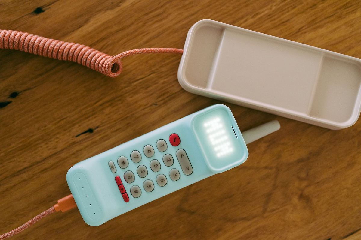 A mint green Waffle Home handset with a coiled orange cord resting on a wooden table, its screen lit.